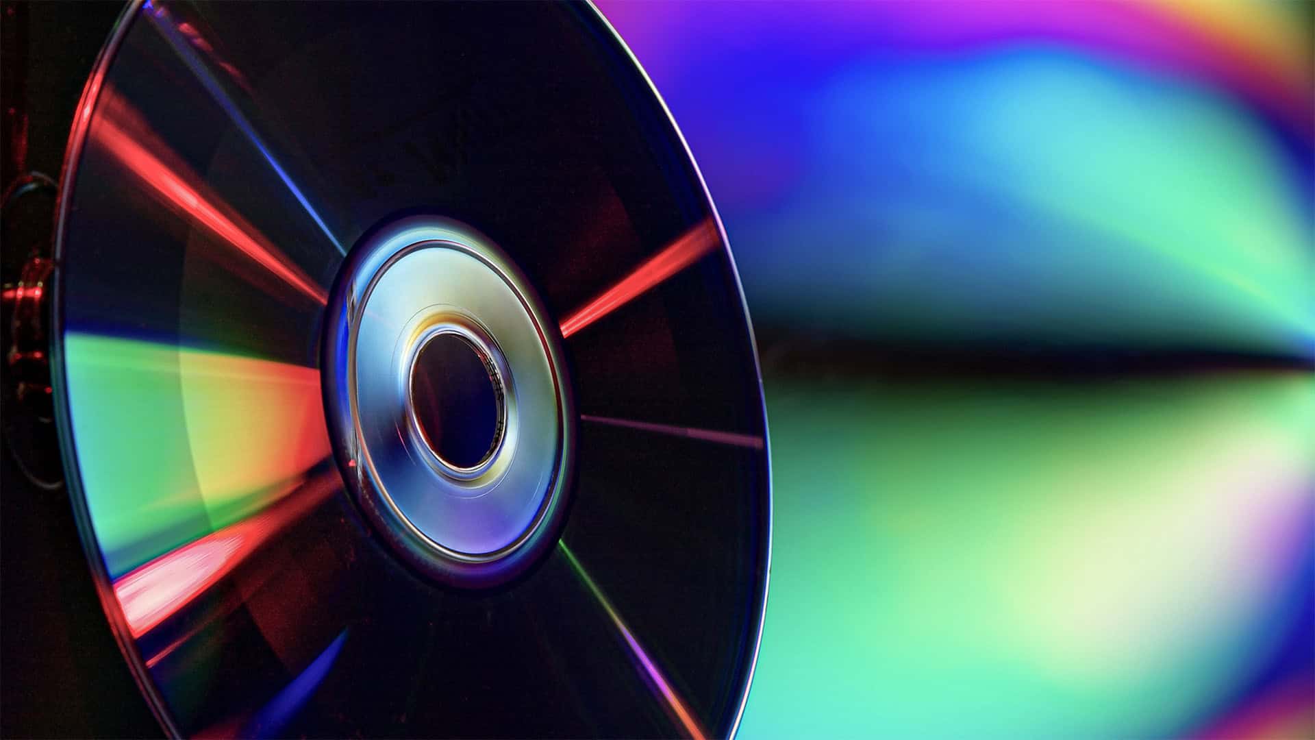 Close-up of a CD reflecting vivid, colorful light patterns, with rainbow hues radiating across and a blurred, vibrant background—perfect for illustrating DVD duplication or CD duplication processes.