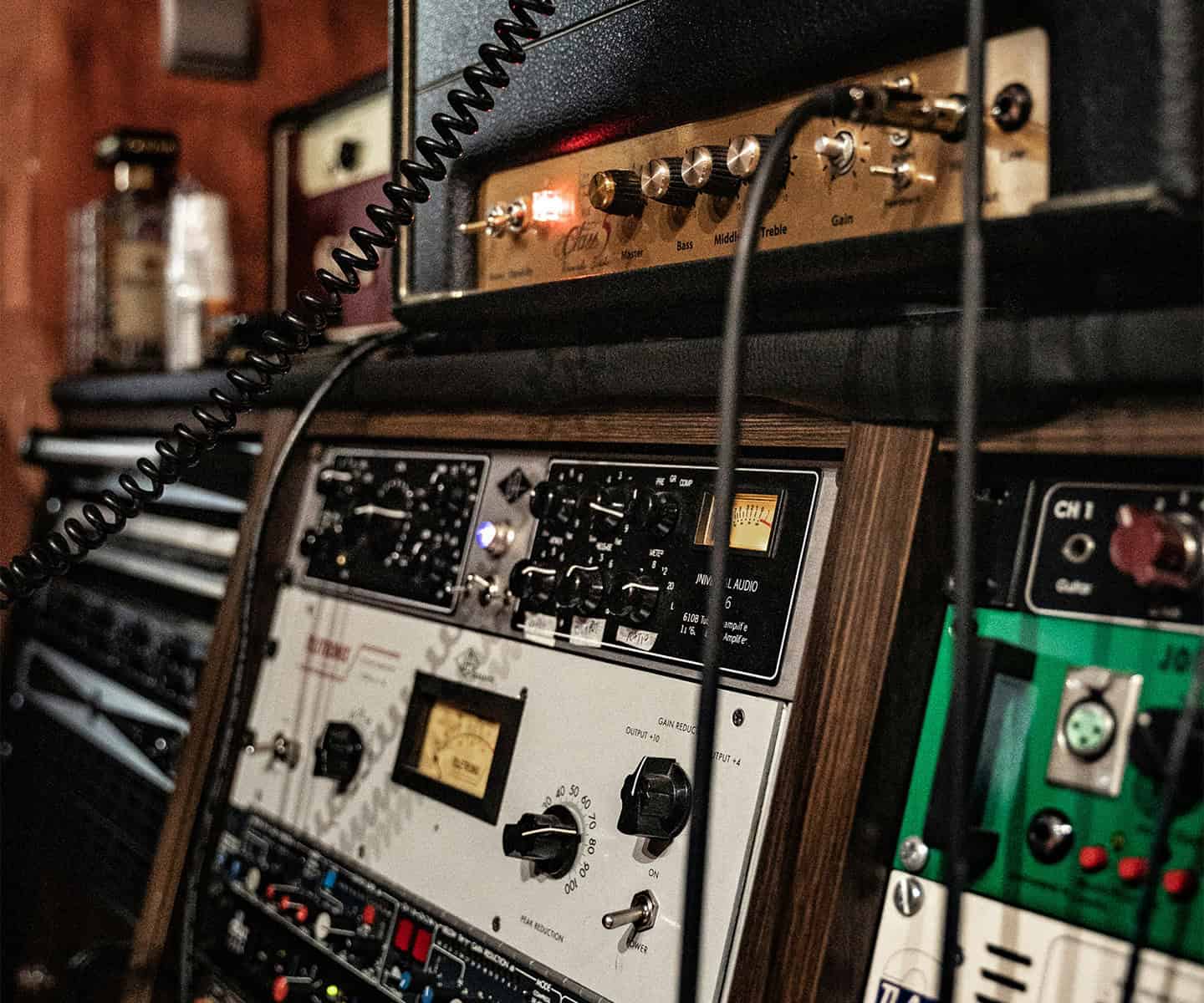 Close-up of various audio equipment, including amplifiers, control panels with dials, switches, and cables, in a music studio or recording setting.